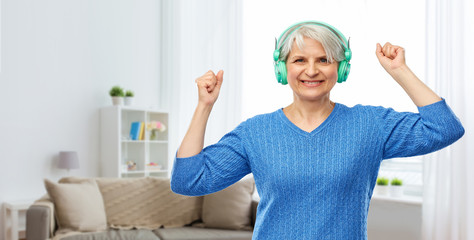 technology and old people concept - smiling senior woman in glasses and headphones listening to music over home living room background