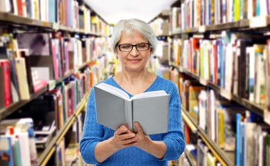 vision, wisdom and old people concept - smiling senior woman in glasses reading book over library background