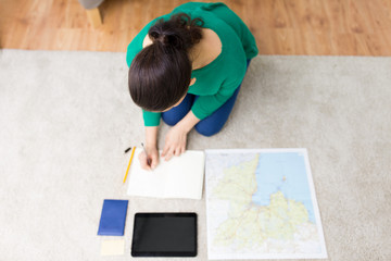tourism, travel and vacation concept - young woman with notebook, tablet computer, passport and map going on trip