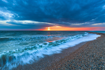Sunset on the beach with long coastline, sun and dramatic sky