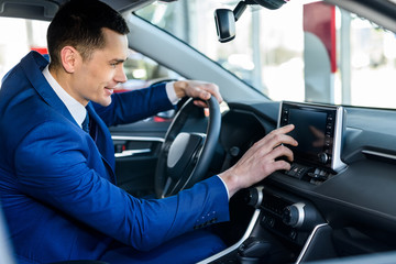 Young and happy businessman sitting in new car in showroom