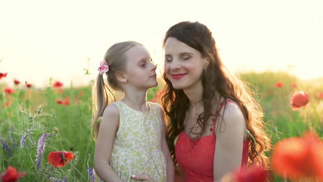Daughter, 6 year old kisses and hugs happy mother in the meadow with poppies and flowers. Happy and touching moments of love mom and daughter. Mother's day