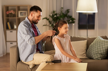 family and people concept - happy father braiding daughter hair at home