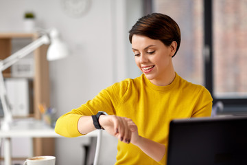 business, technology and time management concept - happy smiling businesswoman using smart watch at office