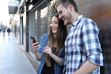 Funny couple checking smart phone content in the street