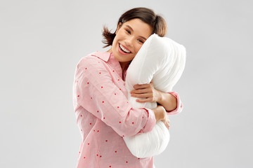 people and bedtime concept - happy young woman in pajama hugging pillow over grey background