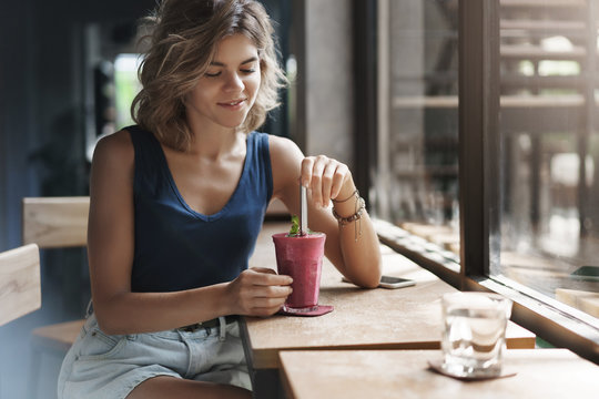 Tender Charming Young Modern Urban Woman Blond Short Hairstyle Sit Window Bar Coffee Table Mixing Smoothie Straw Look Drink Smiling Sensually Enjoy Nice Lunch Break Wait Phone-call