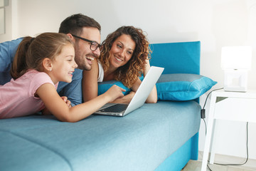 Happy family lies on bed and watching something on laptop.Laughing and fun.