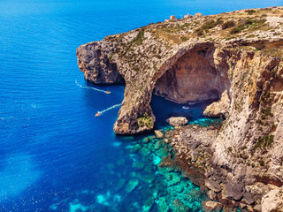 Blue Grotto in Malta. Pleasure boat with tourists runs. Natural arch window in the rock. Aerial top...