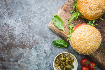 Fresh homemade burger on serving board with spicy sauce and herbs over dark stone background. Top view with copy space