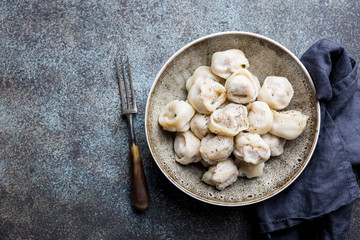 Traditional homemade Russian pelmeni meat dumplings with sour cream and greens over gray background. top view