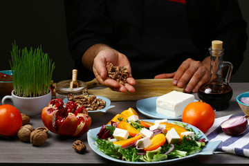 Chef hands cooking Tasty Persimmon and pea shoot salad with walnuts, pomegranate and pumpkin seed