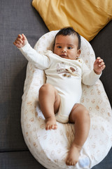 Directly above view of happy excited African baby boy in cute bodysuit lying in safety cocoon on...