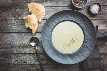Broccoli cream soup in dark bowl on wooden background, top view