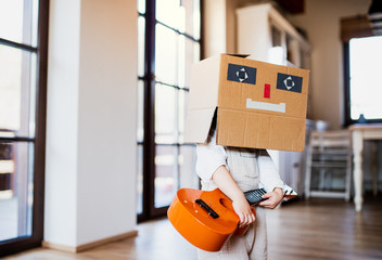 A toddler girl with carboard monster on head playing indoors at home.