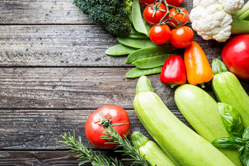 assortment of fresh vegetables cauliflower, broccoli, zucchini and tomatoes on wooden background with space for text
