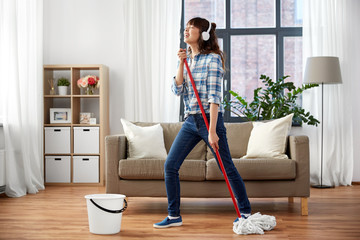 people, housework and housekeeping concept - happy asian woman in headphones with mop and bucket...