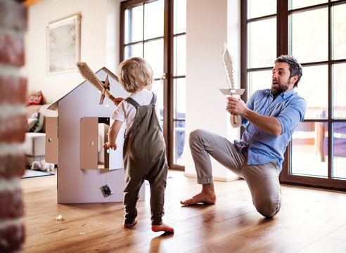 A toddler boy and father with carton swords playing indoors at home.