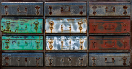 Close-up of a rusty old green white red and grey metal chest of drawers.