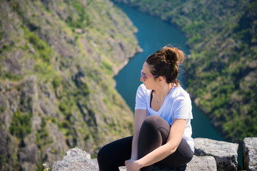 Naklejka na ściany i meble A woman contemplates the incredible Sil Canyon in the Ribeira Sacra from a fabulous viewpoint. The woman is sitting in a rock enjoying the impressive landscape