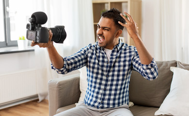 blogging, videoblog and people concept - angry indian male video blogger with camera videoblogging...