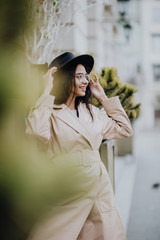 Beautiful girl in a luxurious beige coat, black hat on the street. Young dreamy woman in hat walk in the city. Street fashion look, autumn or spring outfit.