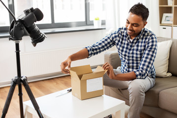 mail delivery, shipment and blogging concept - happy indian male blogger opening parcel box and...