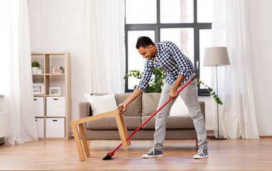 Fototapeta na wymiar cleaning, housework and housekeeping concept - indian man with broom sweeping floor at home