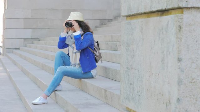 tourist woman in summer holiday, sitting on stairs taking pictures with camera.