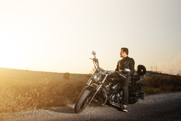 Side view of a young male  biker sitting on the side of the road against sunset while traveling by...