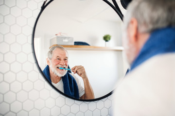 A senior man brushing teeth in bathroom indoors at home. Copy space.