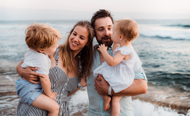 A young family with two toddler children standing on beach on summer holiday.