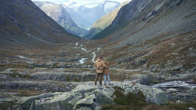 Couple standing on rock in mountains looking epic view to valley