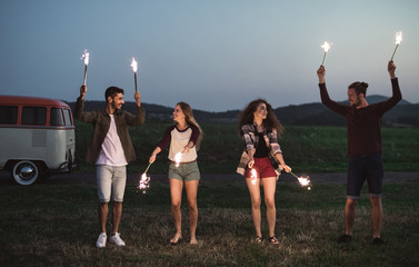 A group of friends with sparklers standing outdoors at dusk.