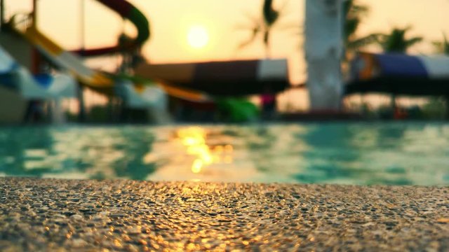 Abstract of The edge of the swimming pool is made of stone on blurry rippled water in swimming pool or water park background at sunset time. can be used for display or montage your products on top.