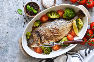 Baked dorado with spices, with broccoli and tomatoes on a concrete background.
