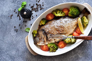 Baked dorado with spices, with broccoli and tomatoes on a concrete background.