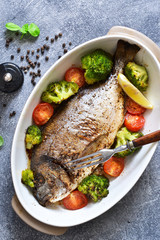 Baked dorado with spices, with broccoli and tomatoes on a concrete background.
