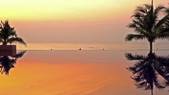 Sun setting over ocean and pool in Tropical scene, palm reflecting on calm pool water