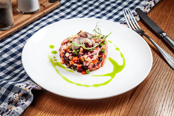 Close up view on modern salad of boiled vegetables with herring served on white plate with green sauce on brown wooden table. Modern chef cuisine. Copy space. the modern vinaigrette