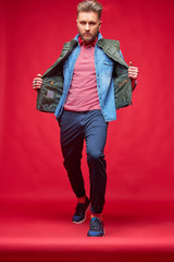 Male model posing in casual clothes. Fashion portrait, studio shot, red background