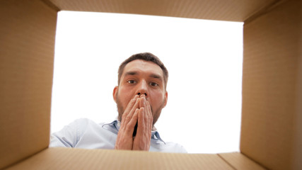 emotions, delivery and surprise concept - shocked man looking into open parcel box, from below