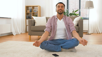 mindfulness, spirituality and music concept - man in headphones meditating in lotus pose at home