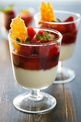 Panna cotta with strawberry sauce, fresh strawberries and candied almonds. Wooden table, morning light, high resolution