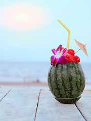Fresh Watermelon smothy.  Take both watermelon balls to make containers and put flower, small umbrella for looking beautiful over white and wood table nealy sea background