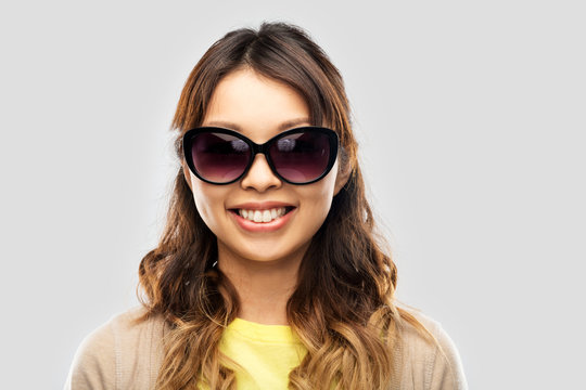 summer fashion, style and eyewear concept - happy smiling young asian woman in sunglasses over grey background