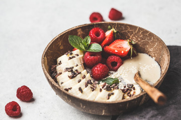 Chia pudding with berries, banana, peanut butter and cocoa nibs in coconut shell bowl.