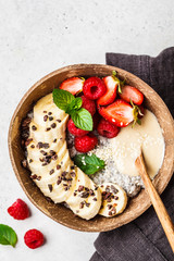 Chia pudding with berries, banana, peanut butter and cocoa nibs in coconut shell bowl, top view.
