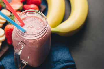 Smoothie with strawberry and banana in the jar at dark background