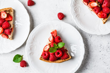 Pieces of berry tart with raspberries, strawberries and cream, top view.